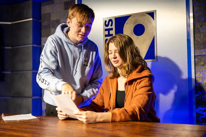 Two students talk over plans at a news desk